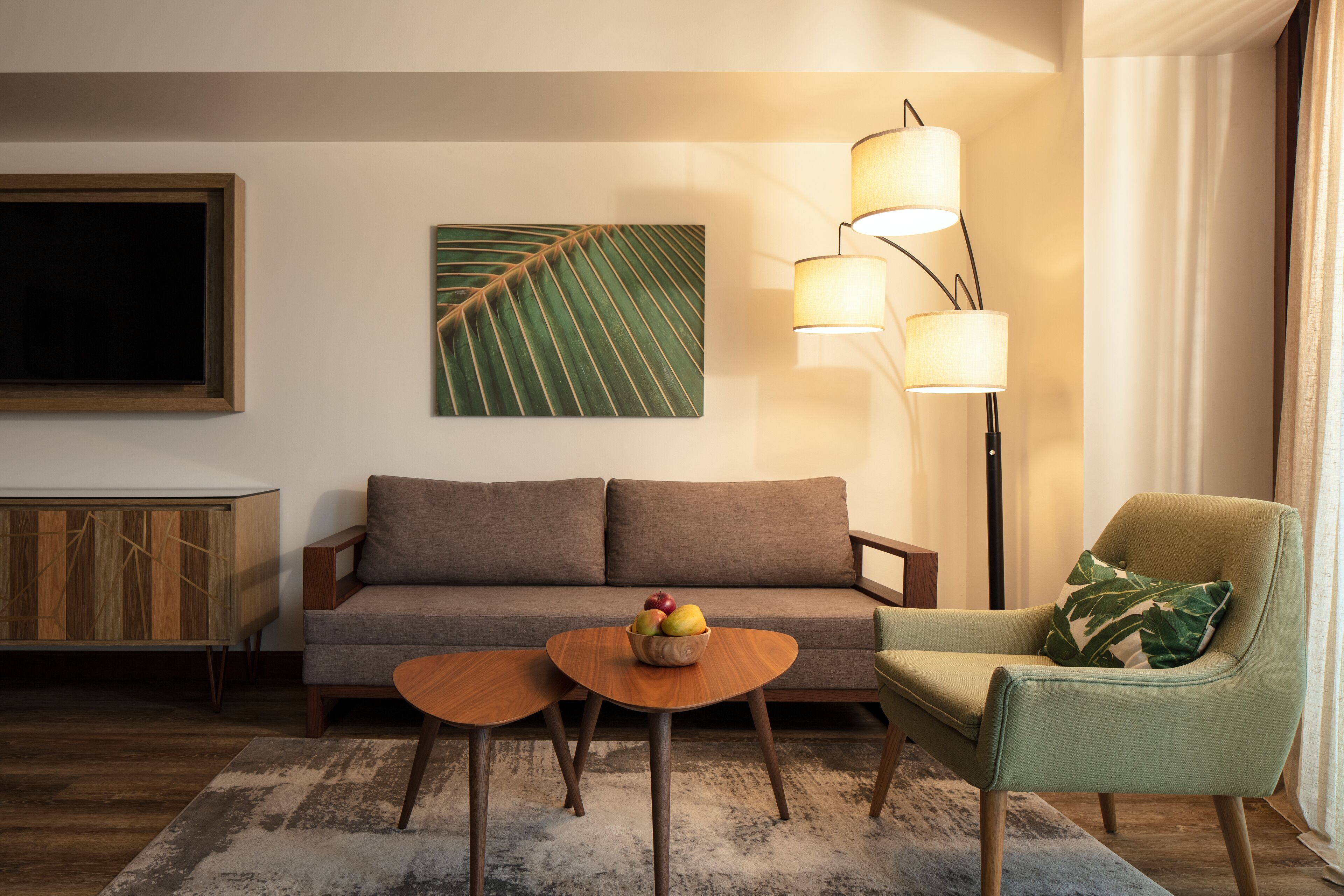 A modern living room with a sofa, a green armchair, a round wooden coffee table with fruit, and a floor lamp.