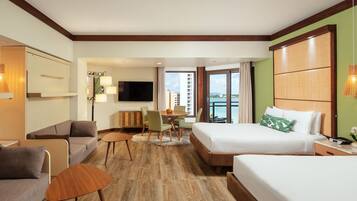 A hotel room with a large bed, a sofa, a dining table with chairs, a TV, and a view of the city.