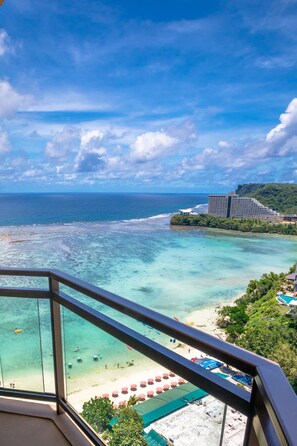 A beach view from a balcony with clear turquoise waters, a sandy beach, and a hotel building in the background. - Dusit Beach Resort Guam (Tamuning)