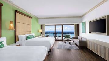 Hotelkamer met twee bedden, een bank, een televisie en een balkon met uitzicht op zee.