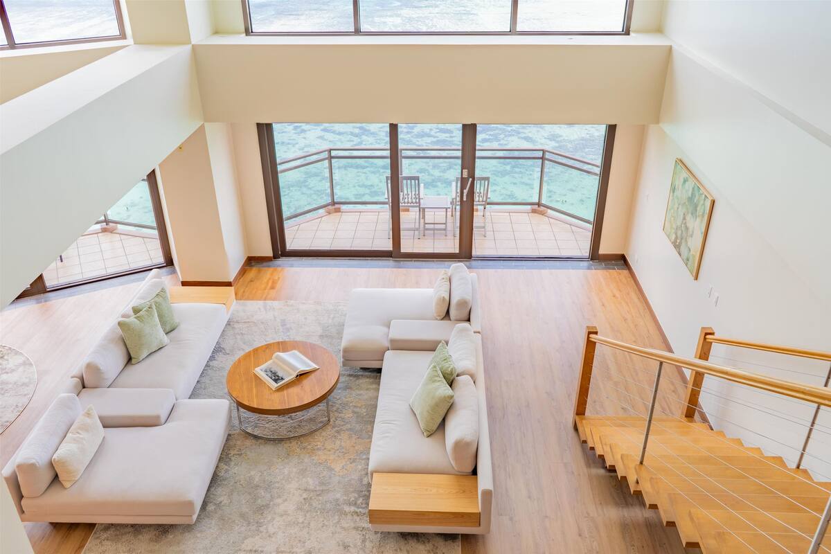 A modern living room with a sofa set, a coffee table, and a view of the sea through large windows.