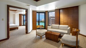 A hotel room with a large window, a sofa, a wooden coffee table, and a chair. - Dusit Beach Resort Guam (Tamuning)