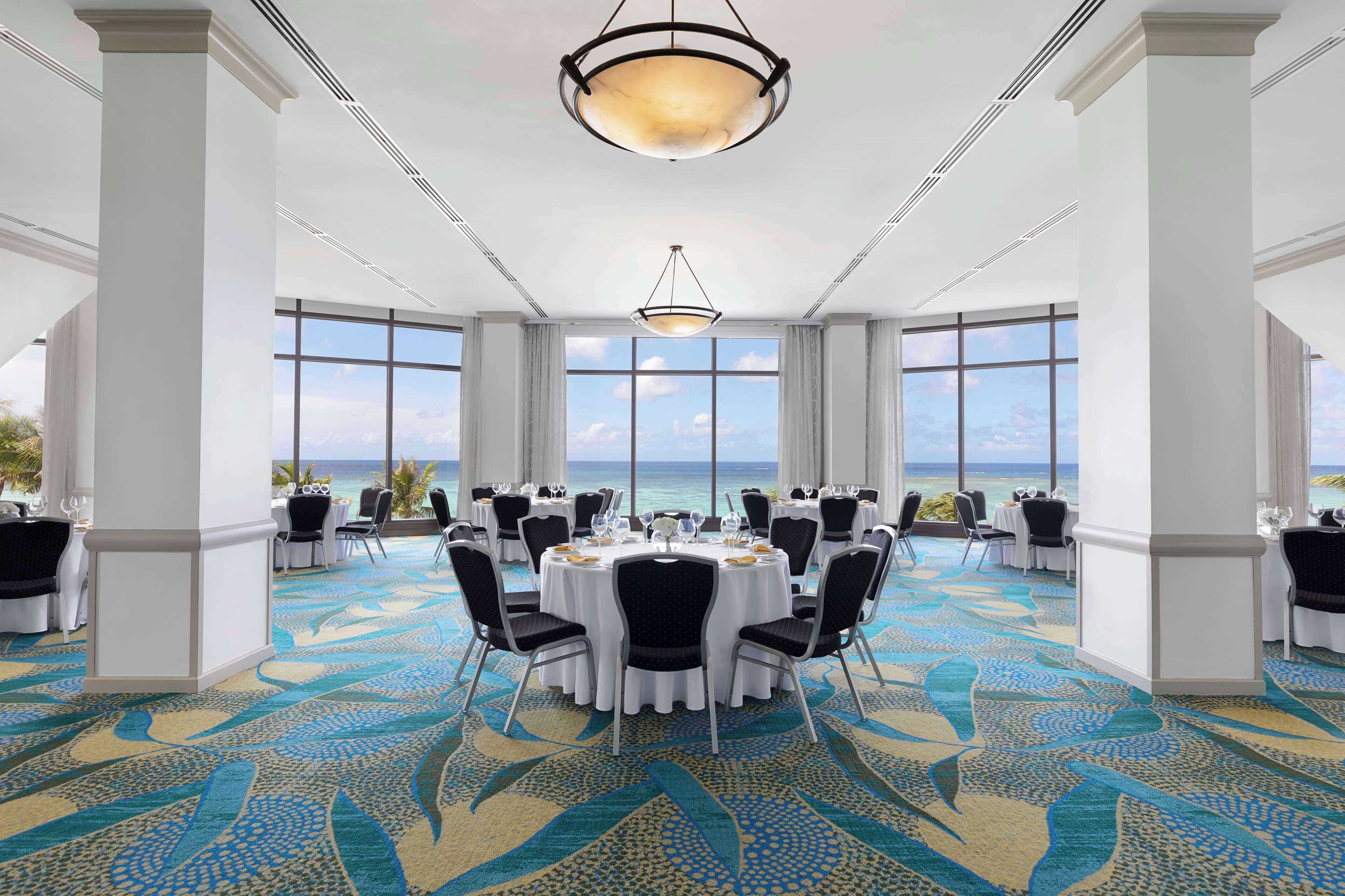 A spacious conference room with round tables, white chairs, and a view of the ocean.