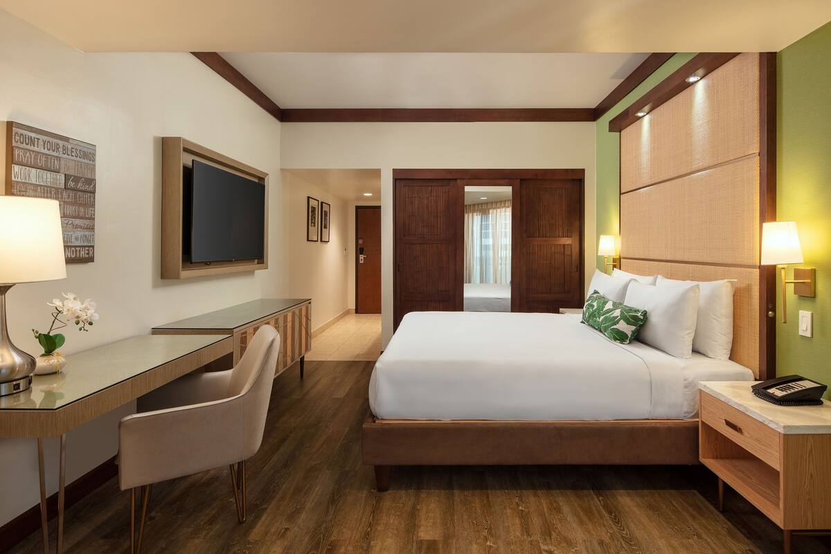 A hotel room with a bed, desk, chair, and a television.