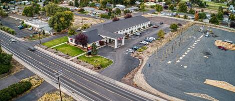 A gas station with a parking lot, a road with a median, and a hilly landscape in the background.