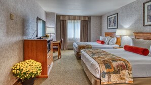 Ett hotellrum med två sängar, ett skrivbord, en tv och en krukväxt.
