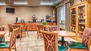 A hotel dining area with wooden tables and chairs, a coffee station, and a television mounted on the wall.