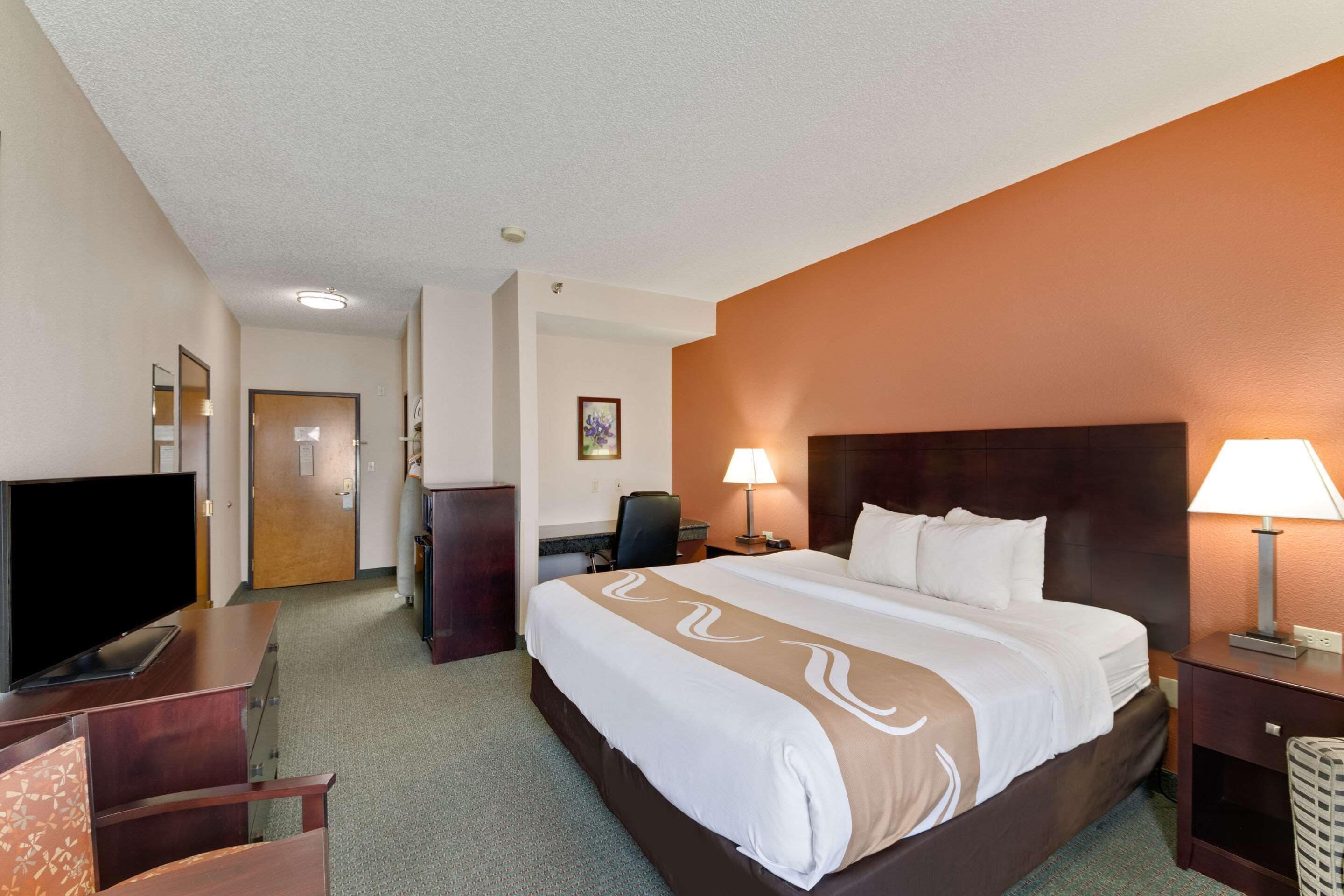 A hotel room with a bed, a desk, a chair, a television, and a lamp.