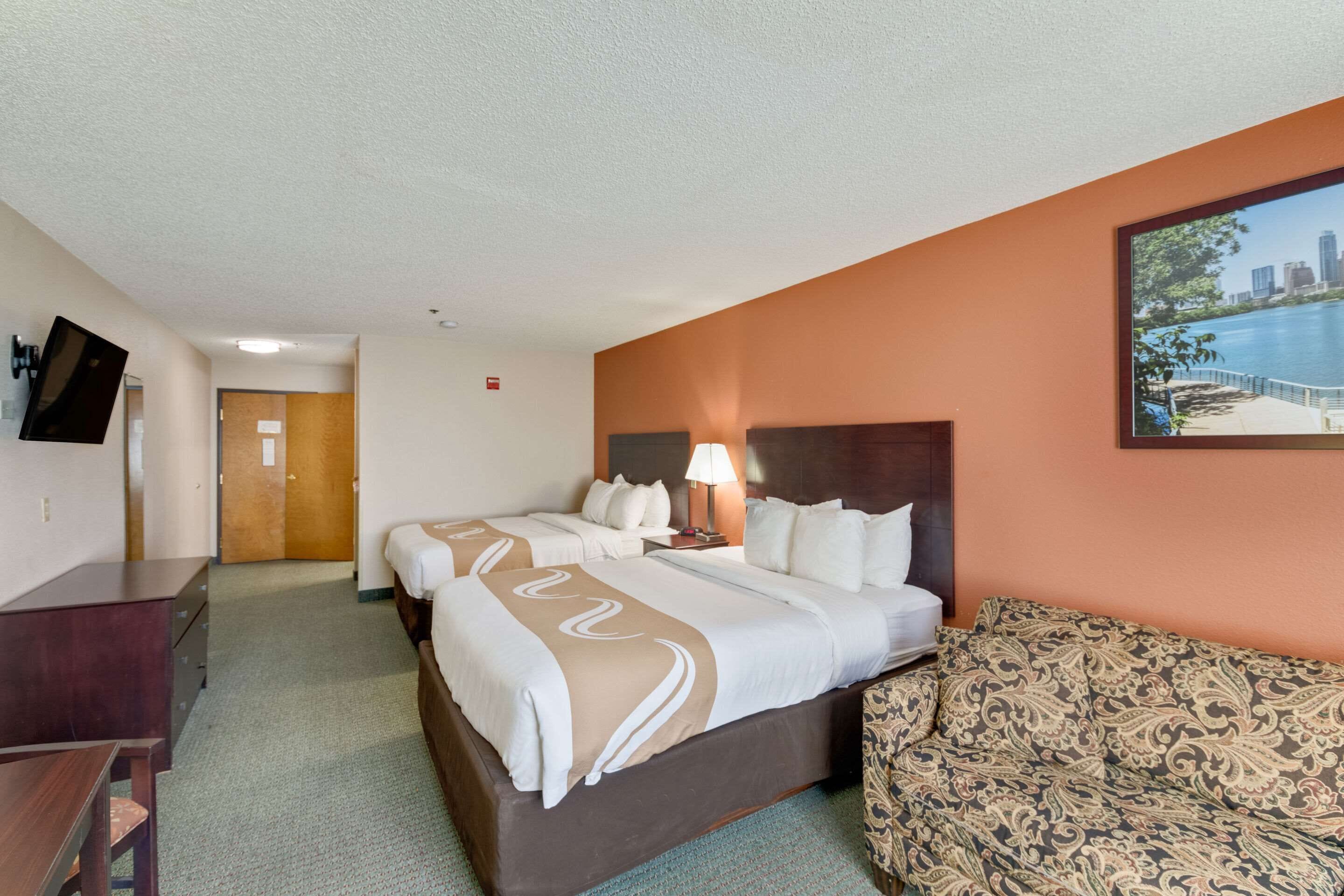Ein Hotelzimmer mit zwei Betten, einem Sofa, einem Fernseher und einem Stadtbild an der Wand.