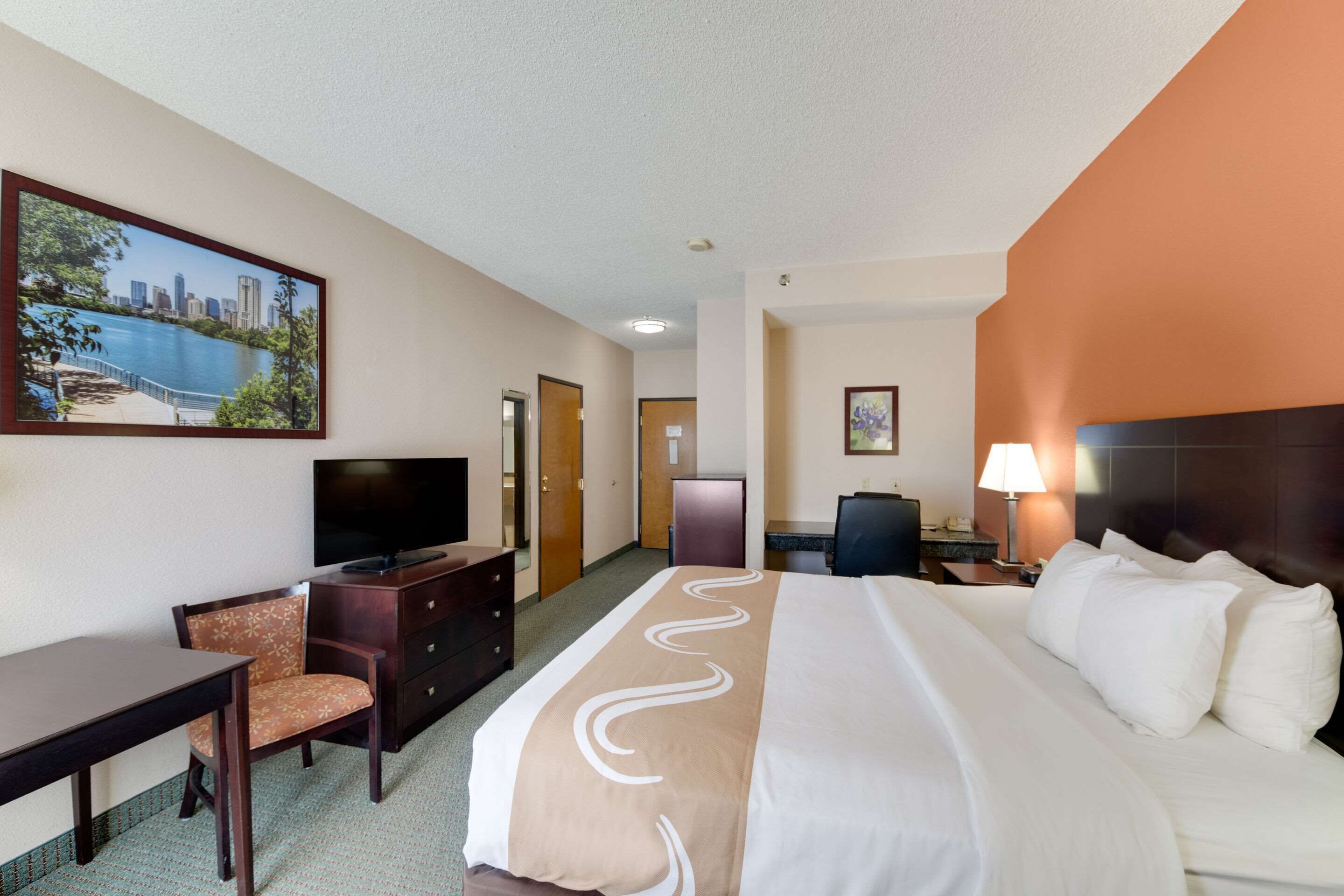 A hotel room with a bed, a desk, a chair, a television, and a painting of a cityscape.
