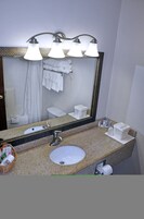 Un baño con encimera de granito, lavamanos, espejo y cortina de ducha.