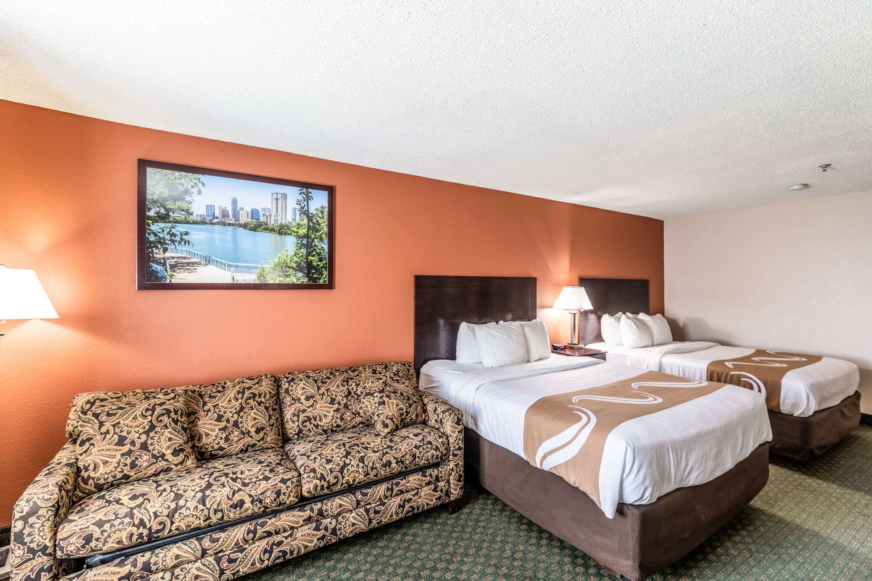 A hotel room with two beds, a sofa, and a cityscape painting on the wall.