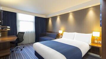 A hotel room with a large bed, a desk with a chair, a small sofa, and two bedside lamps.