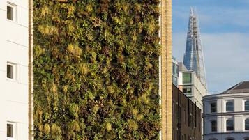 A building with a vertical garden facade and a modern skyscraper in the background.