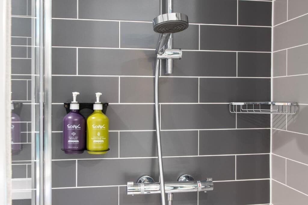 A shower area with a chrome showerhead and two bottles of shampoo on a shelf.