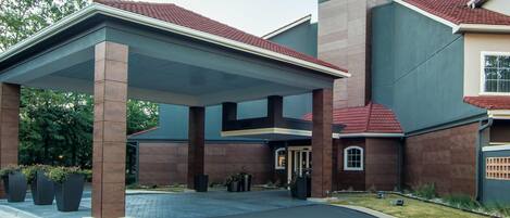 A hotel entrance with a covered waiting area, a prominent sign, and a well-maintained lawn.