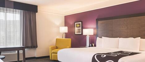 A hotel room with a bed, a desk, a chair, and two lamps.