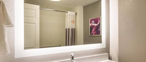 A bathroom with a large mirror, a sink, and a shower area.