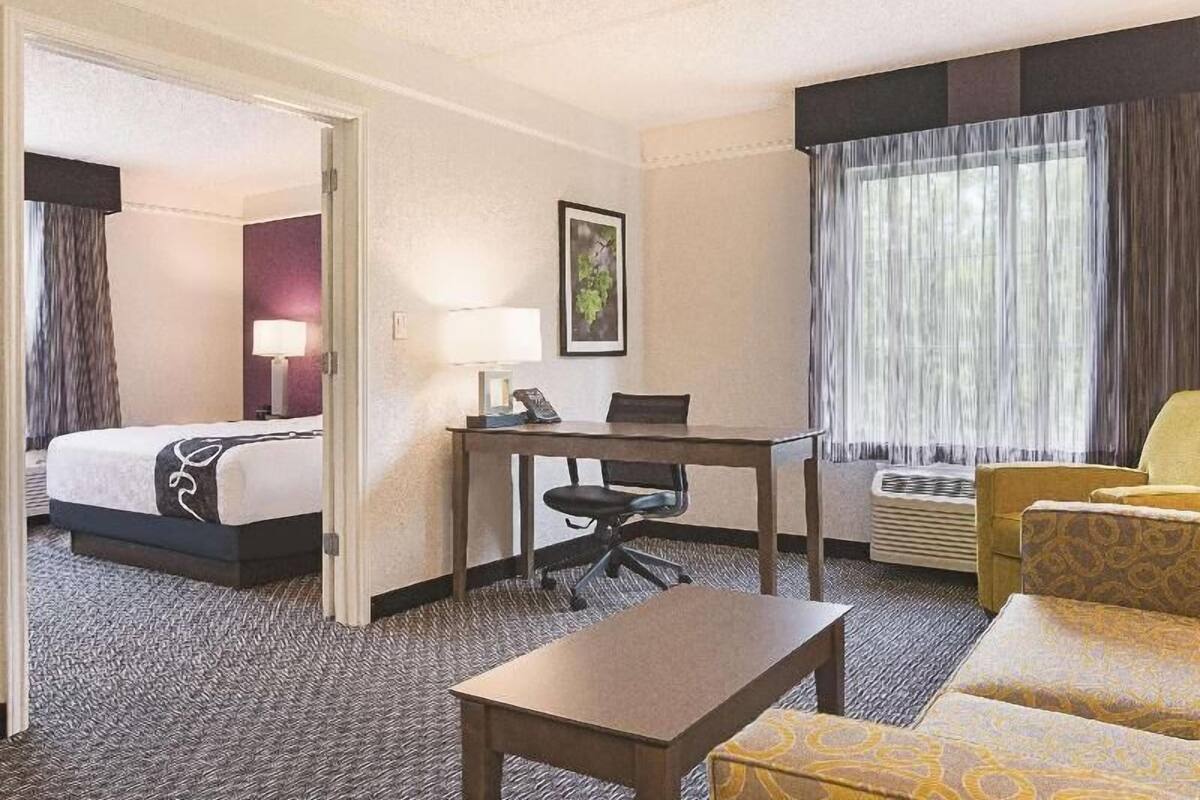A hotel room with a bed, a desk, a chair, a sofa, and a window with curtains.