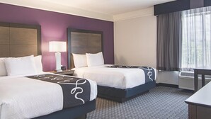 A hotel room with two beds, a desk, a chair, a lamp, and a window with curtains. - La Quinta Inn & Suites by Wyndham Atlanta Perimeter Medical (Atlanta)