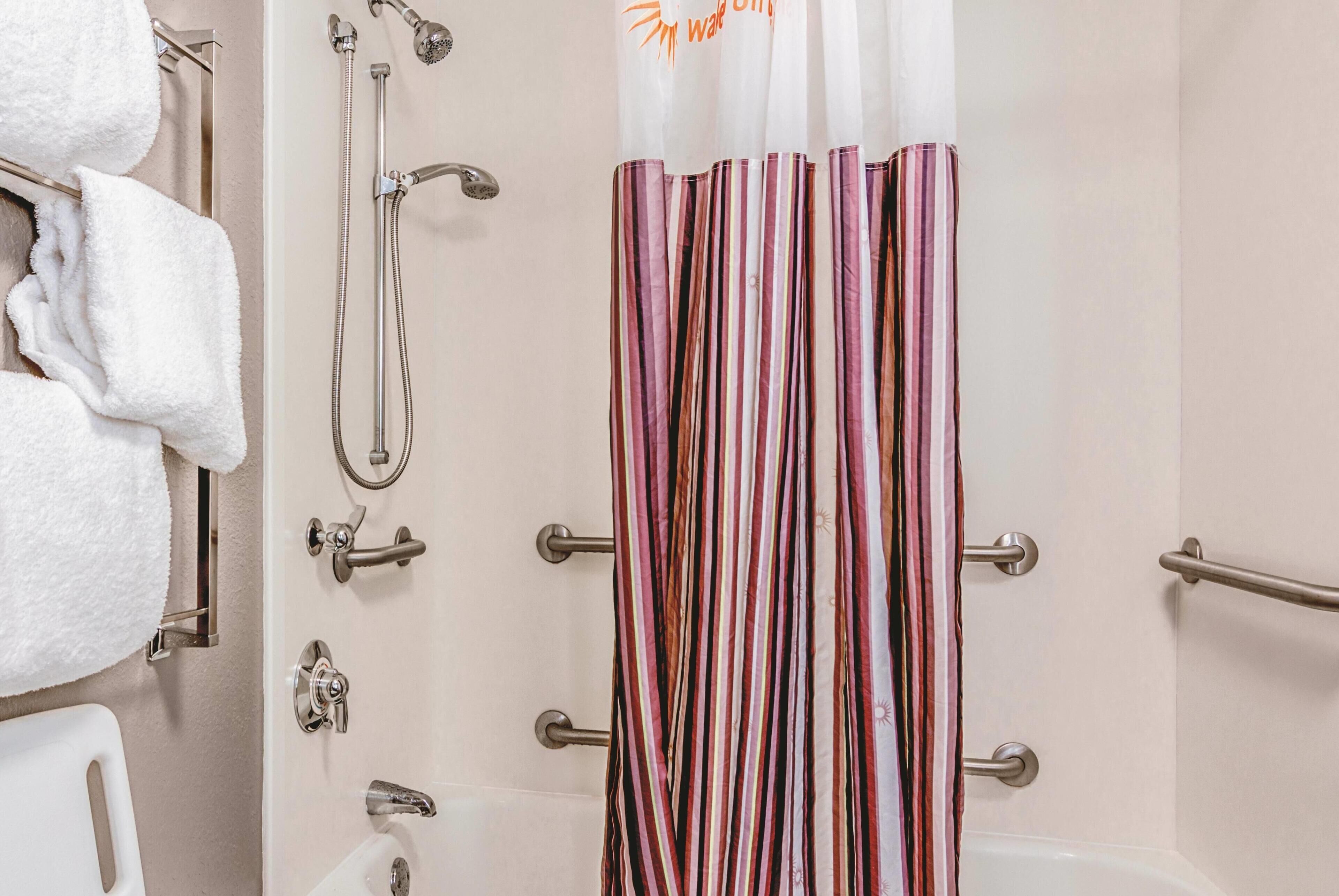 A bathroom with a shower curtain, a towel rack with white towels, and a bathtub.