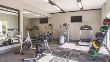 Un gimnasio con varios equipos de ejercicio, incluyendo cintas de correr, elípticas y un estante con balones medicinales.