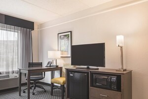 Habitación de hotel con escritorio, silla, televisor, refrigerador, microondas y una ventana con cortinas.