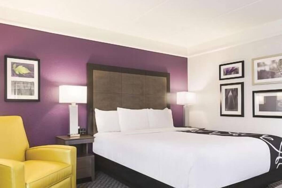 A hotel room with a bed, a nightstand, a lamp, and a chair.