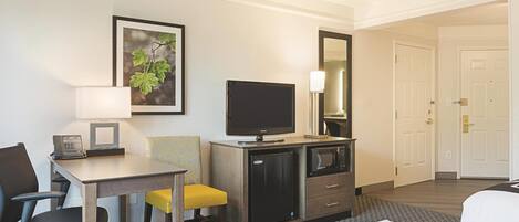 A hotel room with a bed, a desk with a telephone, a television, a microwave, and a small refrigerator.