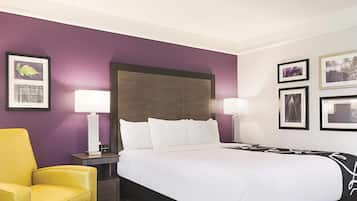A hotel room with a large bed, two bedside lamps, a yellow armchair, and purple walls.