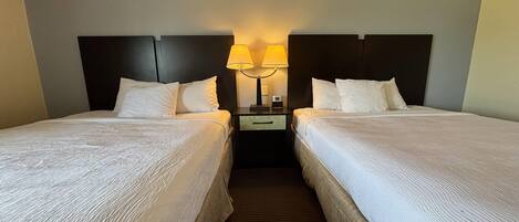 A hotel room with two beds, a nightstand with lamps, and a dark headboard.