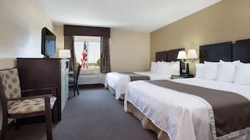 A hotel room with two beds, a desk with a television, a chair, and a view of the outdoors.