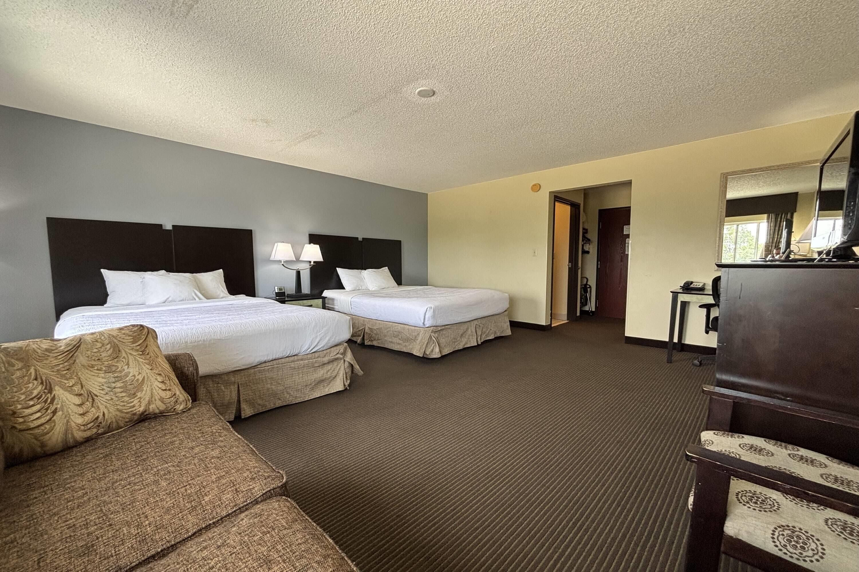 A hotel room with two beds, a sofa, a desk, and a mirror.