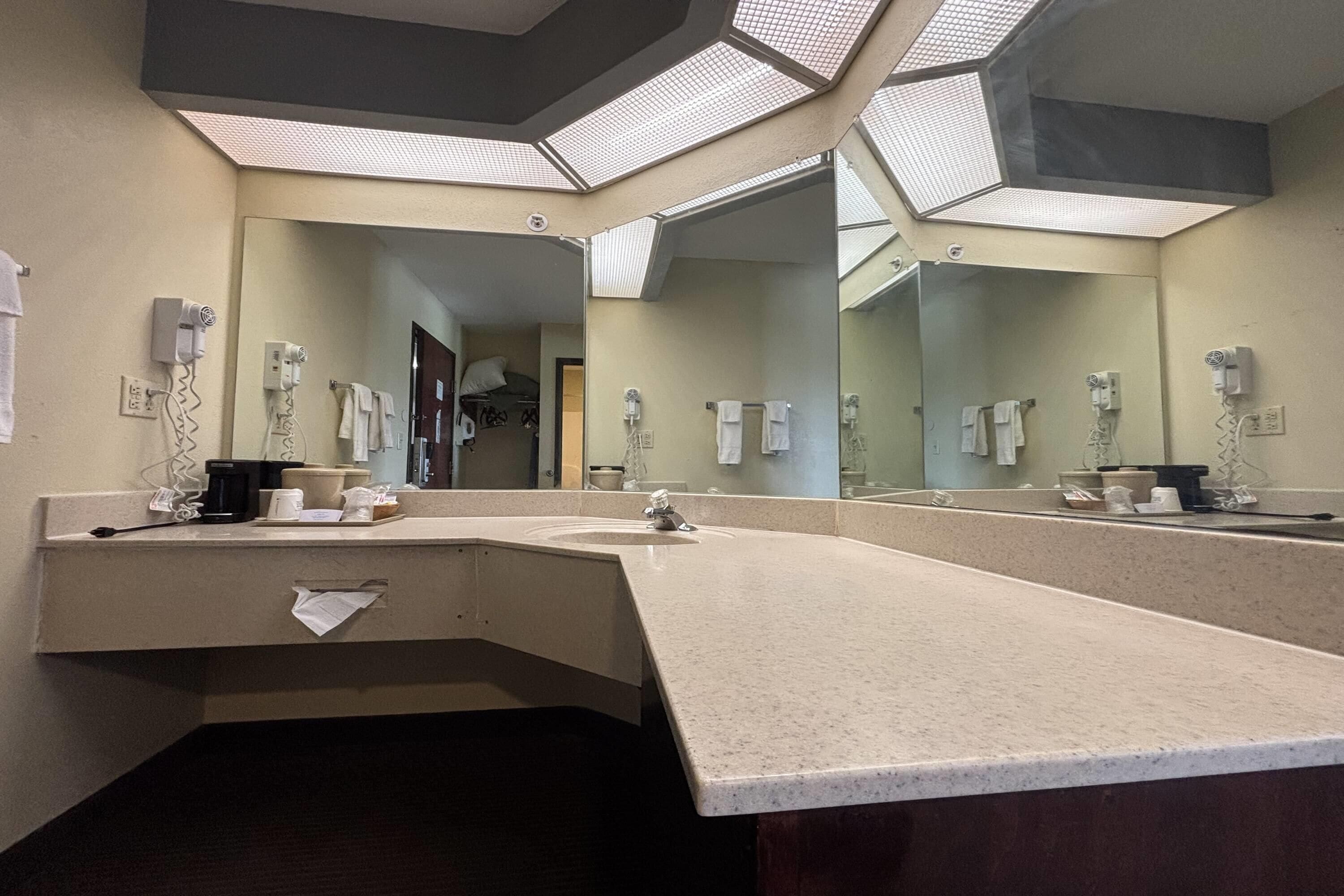 Un baño de hotel con un espejo grande, varios secadores de pelo y un lavamanos.