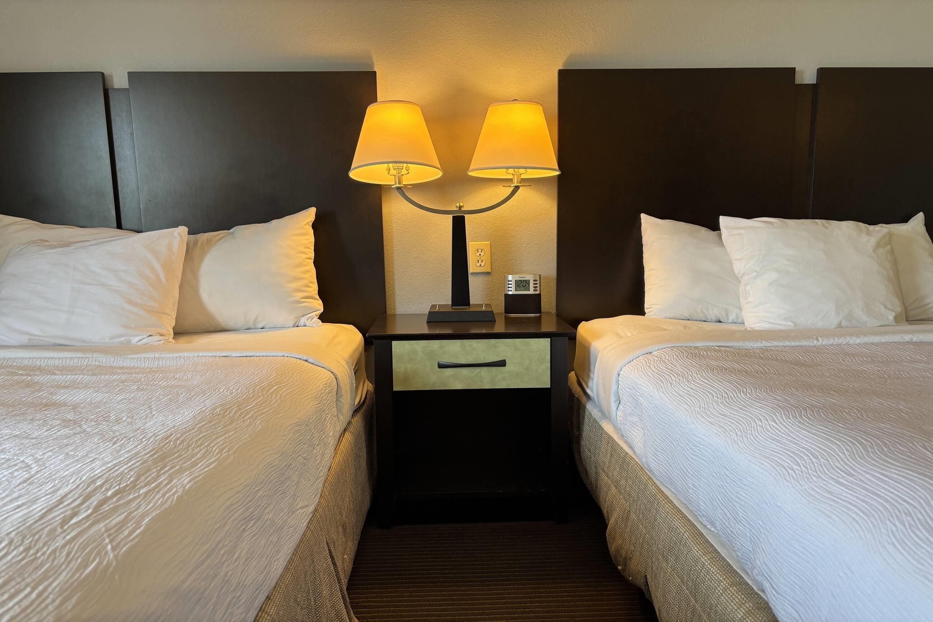 Ein Hotelzimmer mit zwei Betten, einem Nachttisch mit Lampe und einem Thermostat.