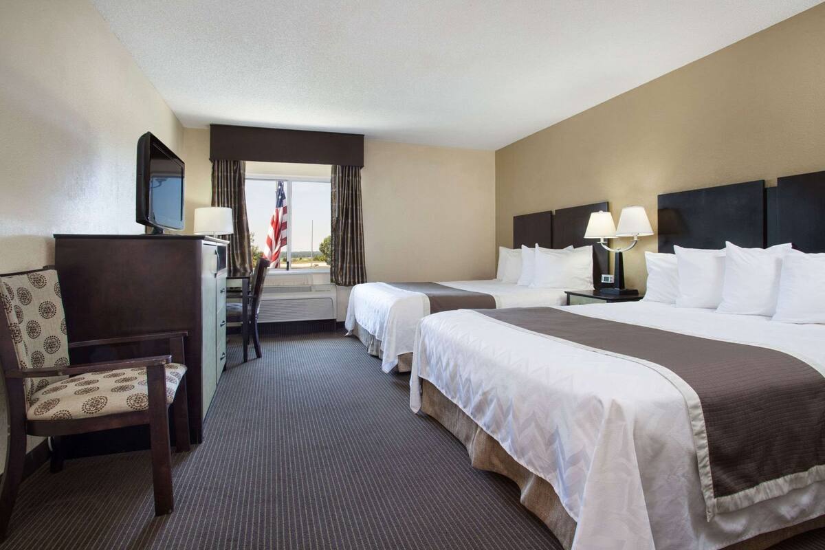 A hotel room with two beds, a desk, a chair, a television, and a window with curtains.