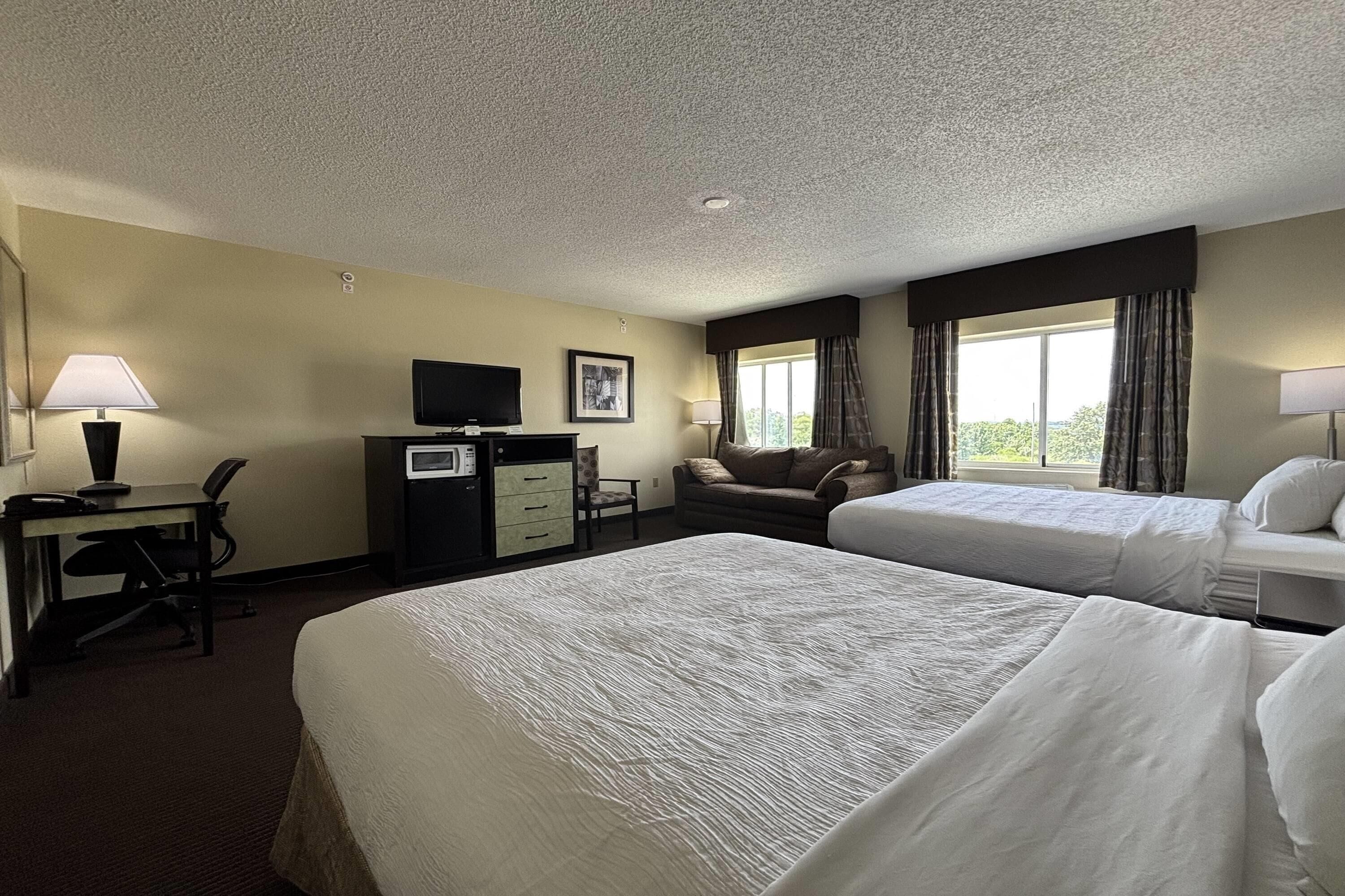 A hotel room with two beds, a desk with a computer, a TV, and a window with curtains.