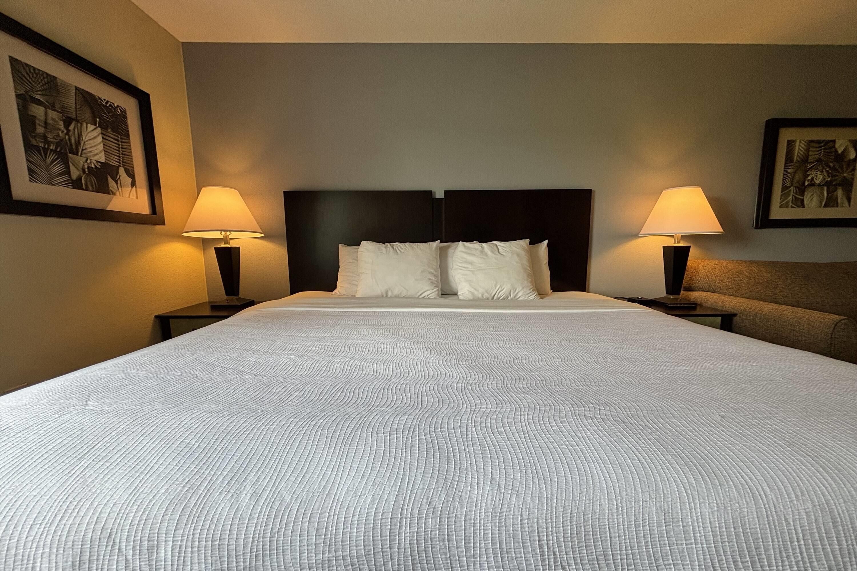 A hotel room with a large bed, two bedside tables with lamps, and framed artwork on the walls.