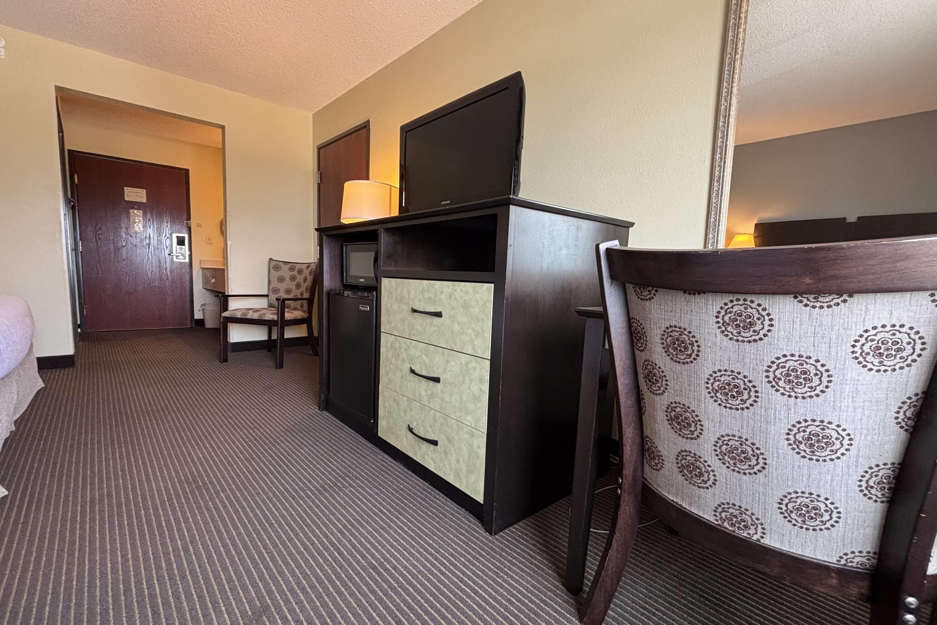 A hotel room with a desk, chair, and a television.