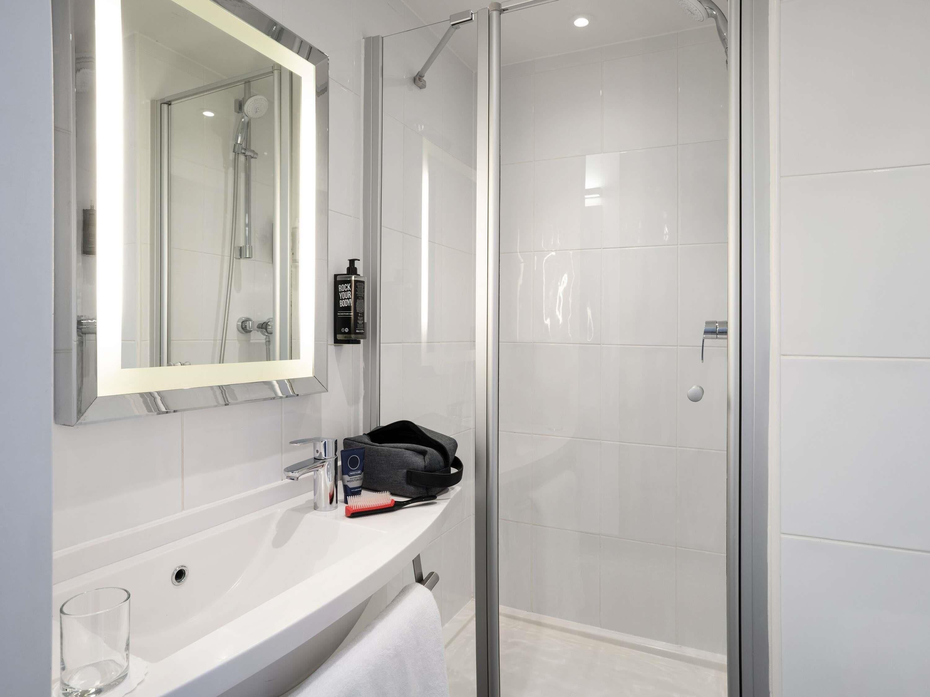 Een moderne badkamer met een douchecabine van glas, een witte wastafel, een grote spiegel en een handdoekhouder.