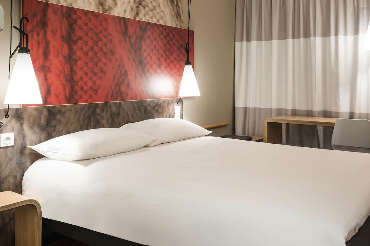 Ett hotellrum med en säng, sänglampor, ett skrivbord och en stol.