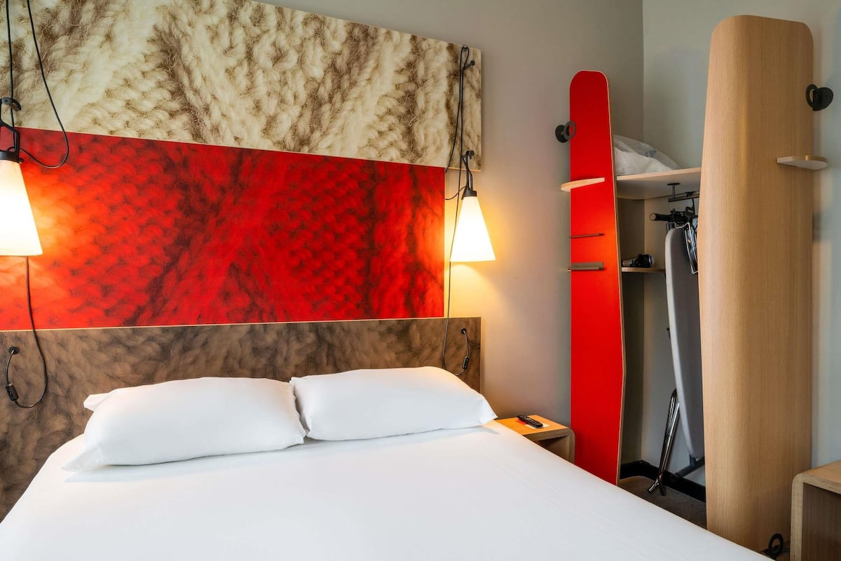 Ett hotellrum med en säng, två sänglampor, en röd duschdraperi och en väggpanel av trä.