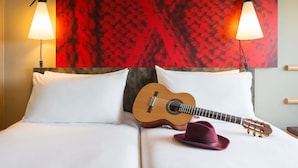 Ein Bett mit weißer Bettwäsche, einer Gitarre und einem Hut darauf.