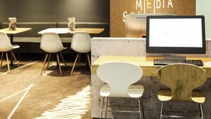 Ein moderner Arbeitsplatz mit Computer, Stühlen, Tischen und einer Wand mit der Aufschrift 'BUSINESS NETWORK MEDIA'.