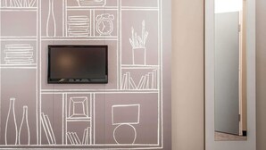 Ein modernes Zimmer mit einem Flachbildfernseher an einer Tafelwand, einer Tür mit Spiegel und einem Flur.