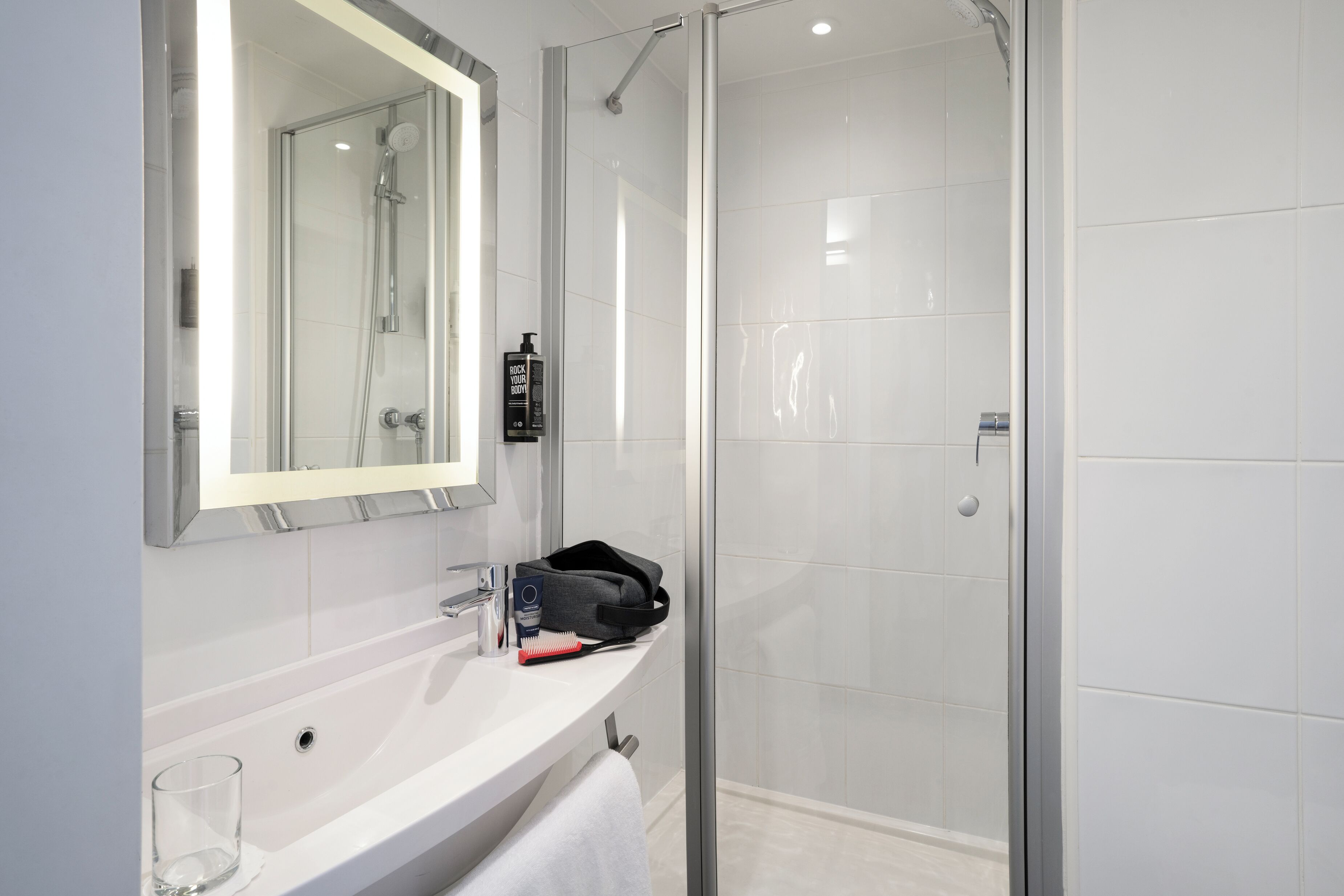 A modern bathroom with a glass shower enclosure, a white sink, a mirror, and a towel rack.