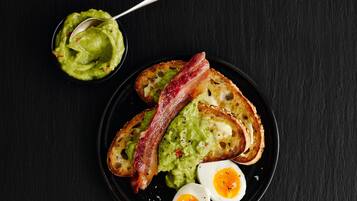 A plate with toast, guacamole, bacon, and a boiled egg.