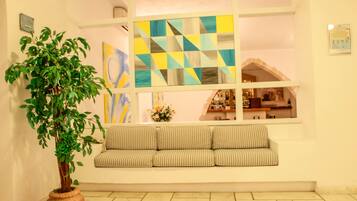 A room with a large window, a potted plant, a striped sofa, and a tiled floor.