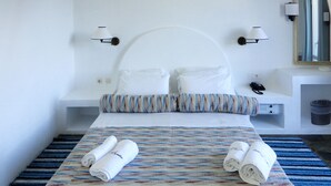 A neatly made bed with patterned bedding and rolled towels, a bedside table with a lamp, and a wall-mounted mirror.