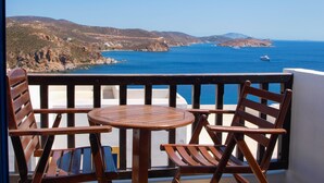 A balcony with wooden furniture overlooking a coastal landscape with clear blue waters and distant hills.